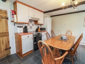 A kitchen with a stove, oven, coffee maker, and a dining table with chairs. - Honey Cottage (Ilfracombe)