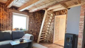 A cozy room with a wooden ceiling, a sofa, a small table, a fireplace, and a wooden ladder. - 4 Star Holiday Home in Sodra vi (Sodra Vi)
