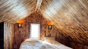 A bedroom with a sloped ceiling, wooden walls, a bed, two wall-mounted lamps, and a window. - 4 Star Holiday Home in Sodra vi (Sodra Vi)