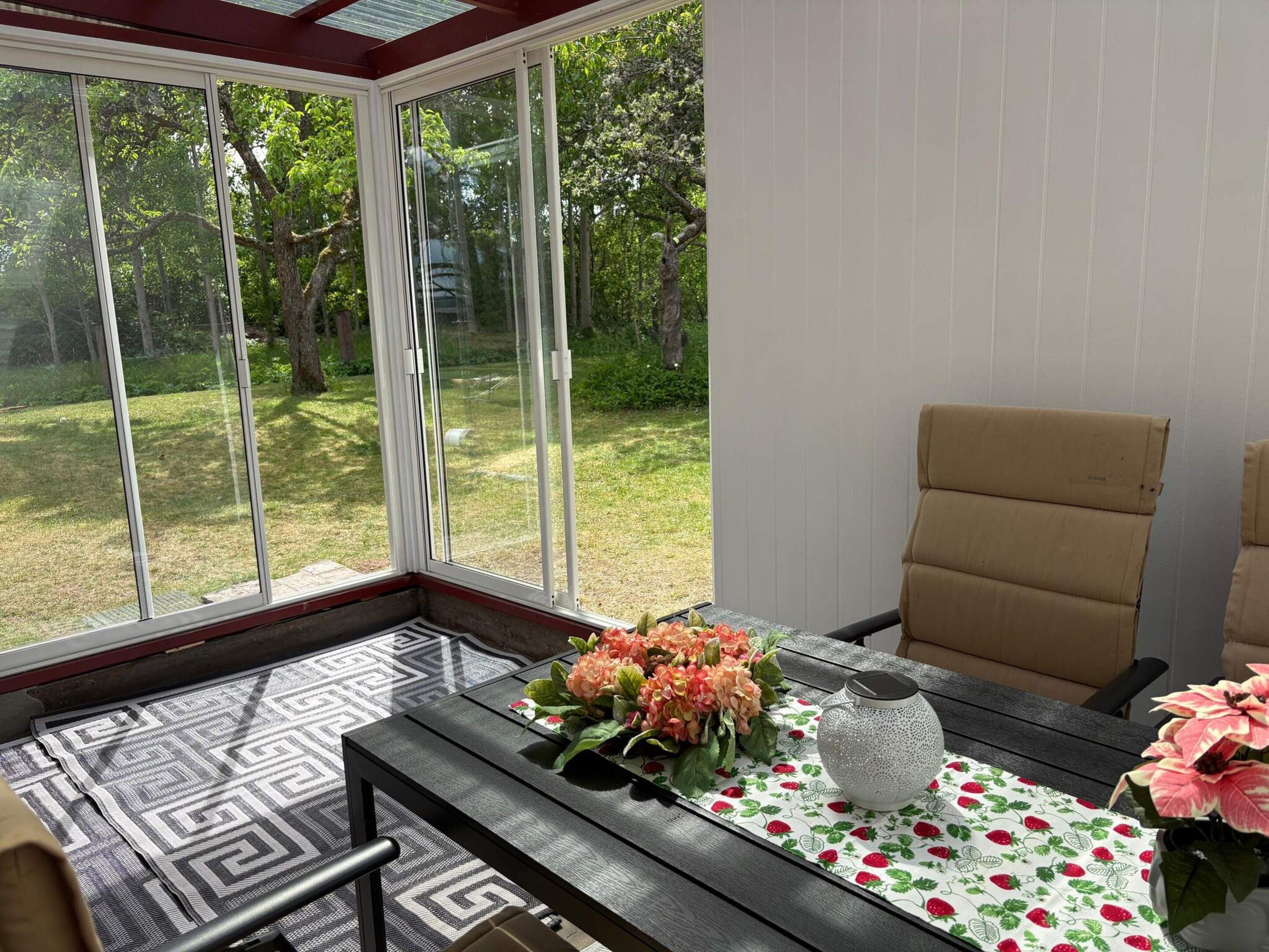 Une véranda avec une porte vitrée, un tapis à motifs, une table ornée de fleurs et une chaise.