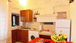 Cozinha compacta com armários de madeira, máquina de lavar, geladeira e mesa de jantar com toalha vermelha.