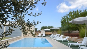 Piscina com espreguiçadeiras e guarda-sóis, cercada por vegetação e um céu claro.