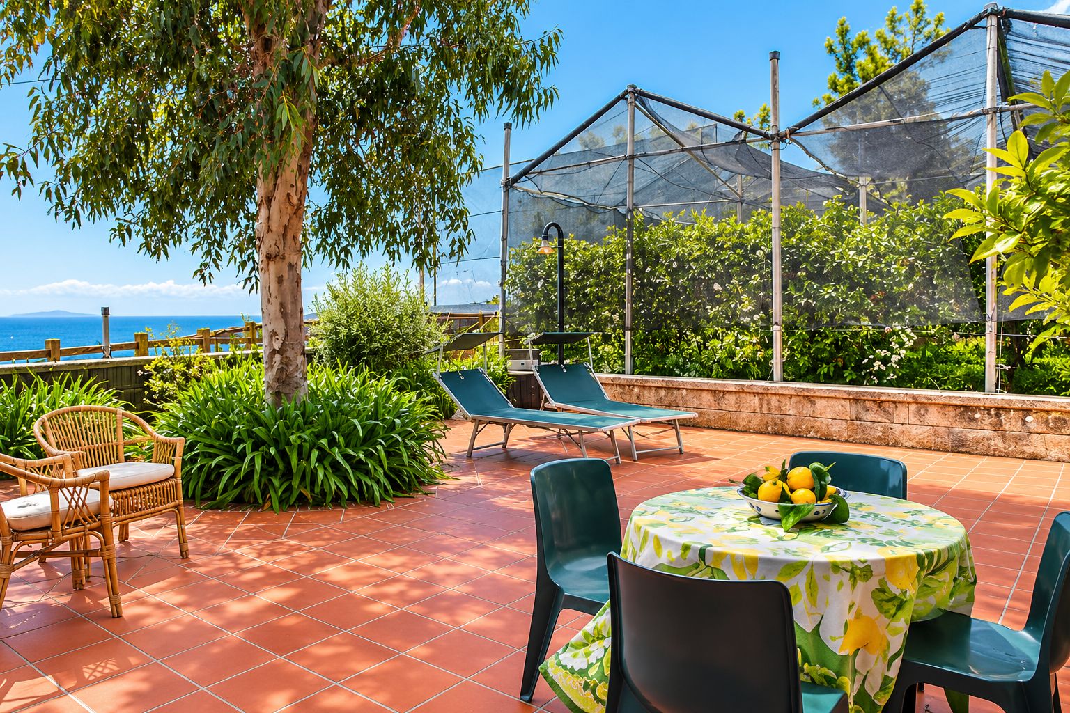 An outdoor patio with a table set for dining, lounge chairs, and a view of the sea.