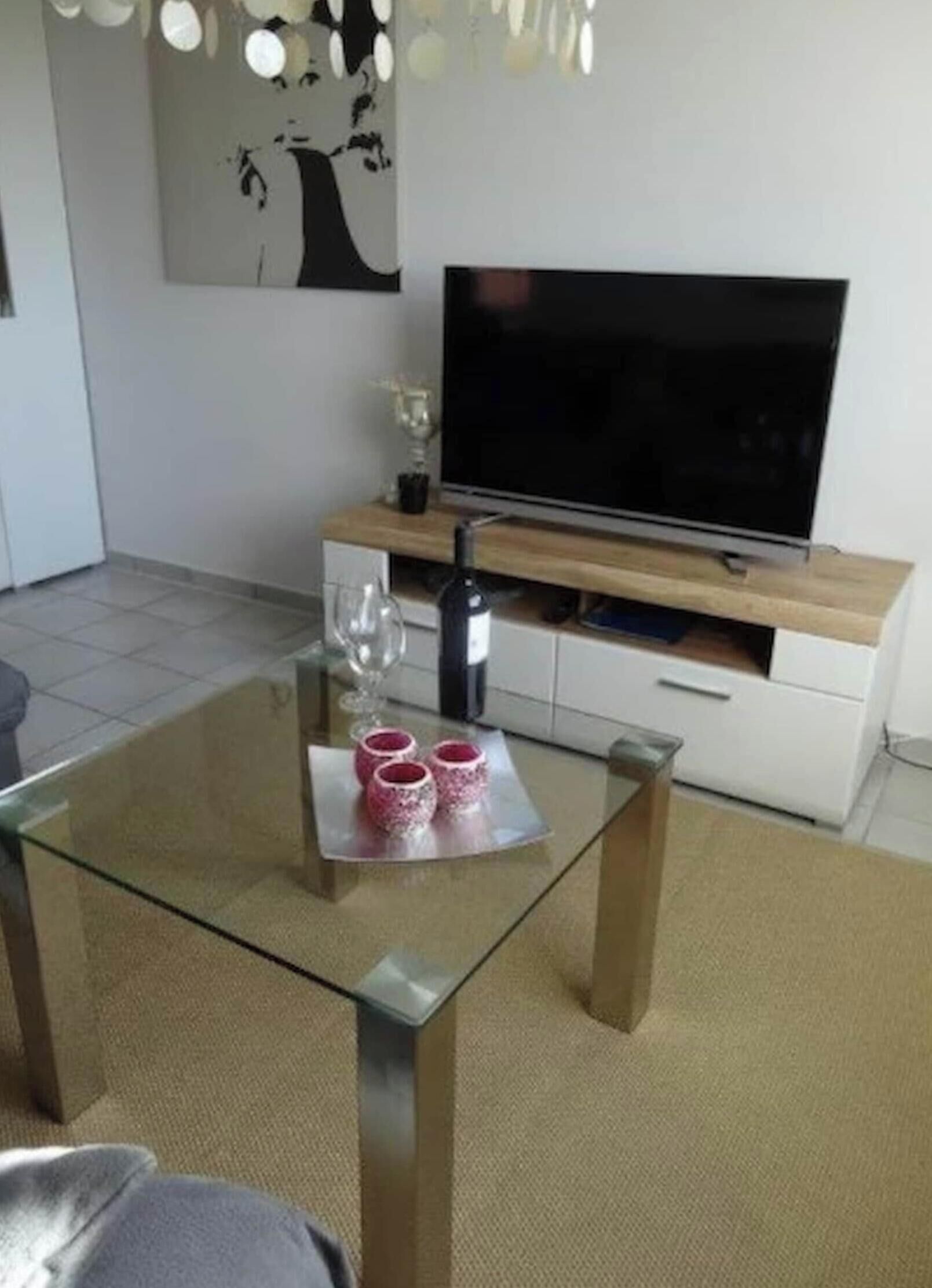 Uma sala de estar moderna com uma mesa de centro de vidro, uma TV de tela plana, um armário branco e um quadro na parede.