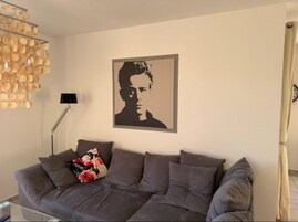 Ein Wohnzimmer mit grauem Sofa, einer schwarzen Stehlampe und einem gerahmten Porträt an der Wand.