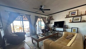 Uma sala de estar com sofá, mesa de centro, televisão e ventilador de teto.