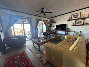 A living room with a sofa, a coffee table, a television, and a ceiling fan. - Mision Los Sahuaros #72 - 2BR with Rooftop Deck (San Felipe)