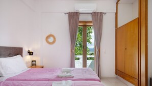 A bedroom with a bed, a wardrobe, a nightstand, a wall-mounted air conditioner, and a view of greenery outside.