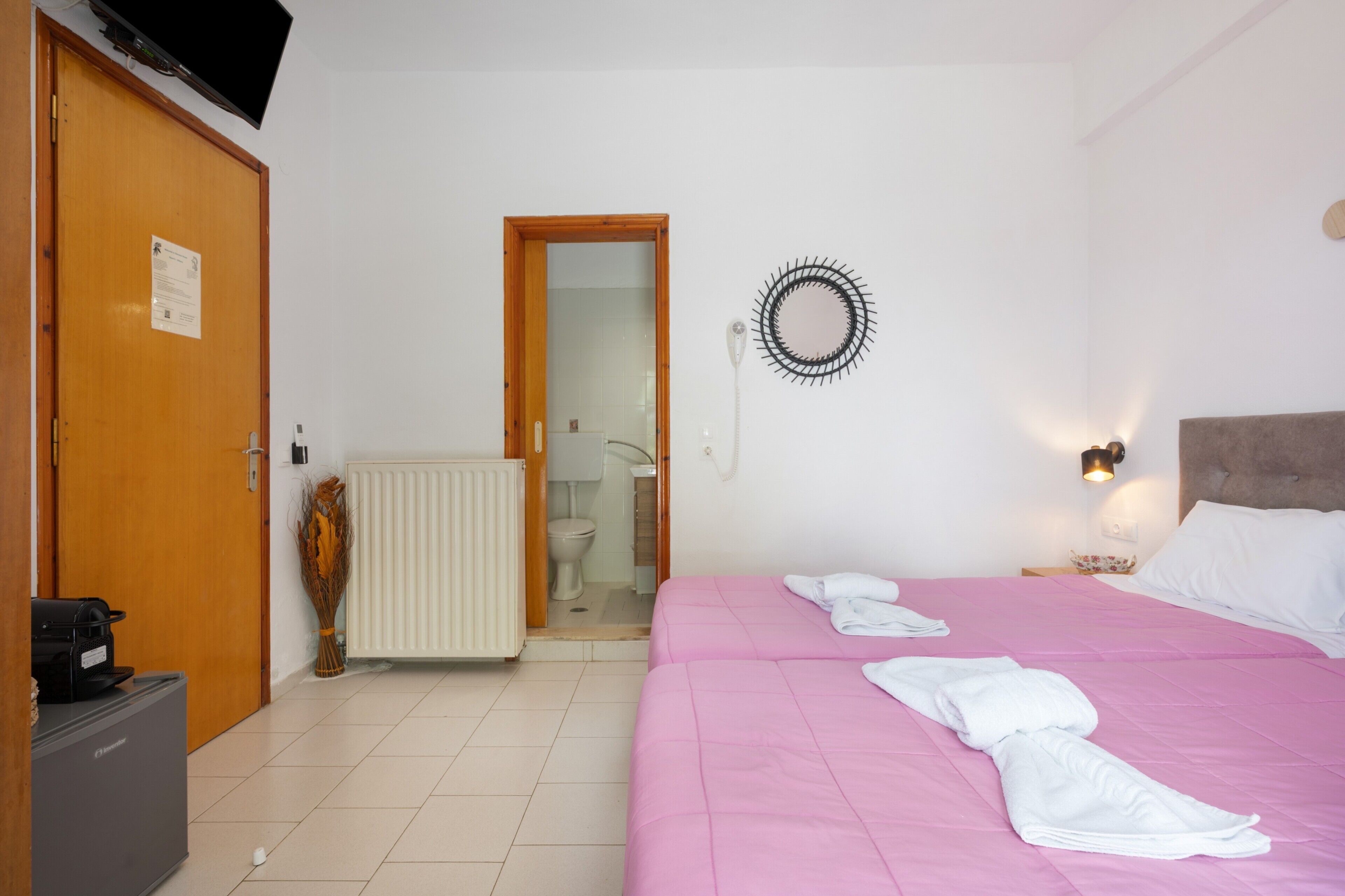 A hotel room with a bed, a radiator, a door, and a television mounted on the wall.