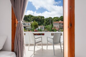 Un balcón con dos sillas, una cama y vistas a edificios y árboles.