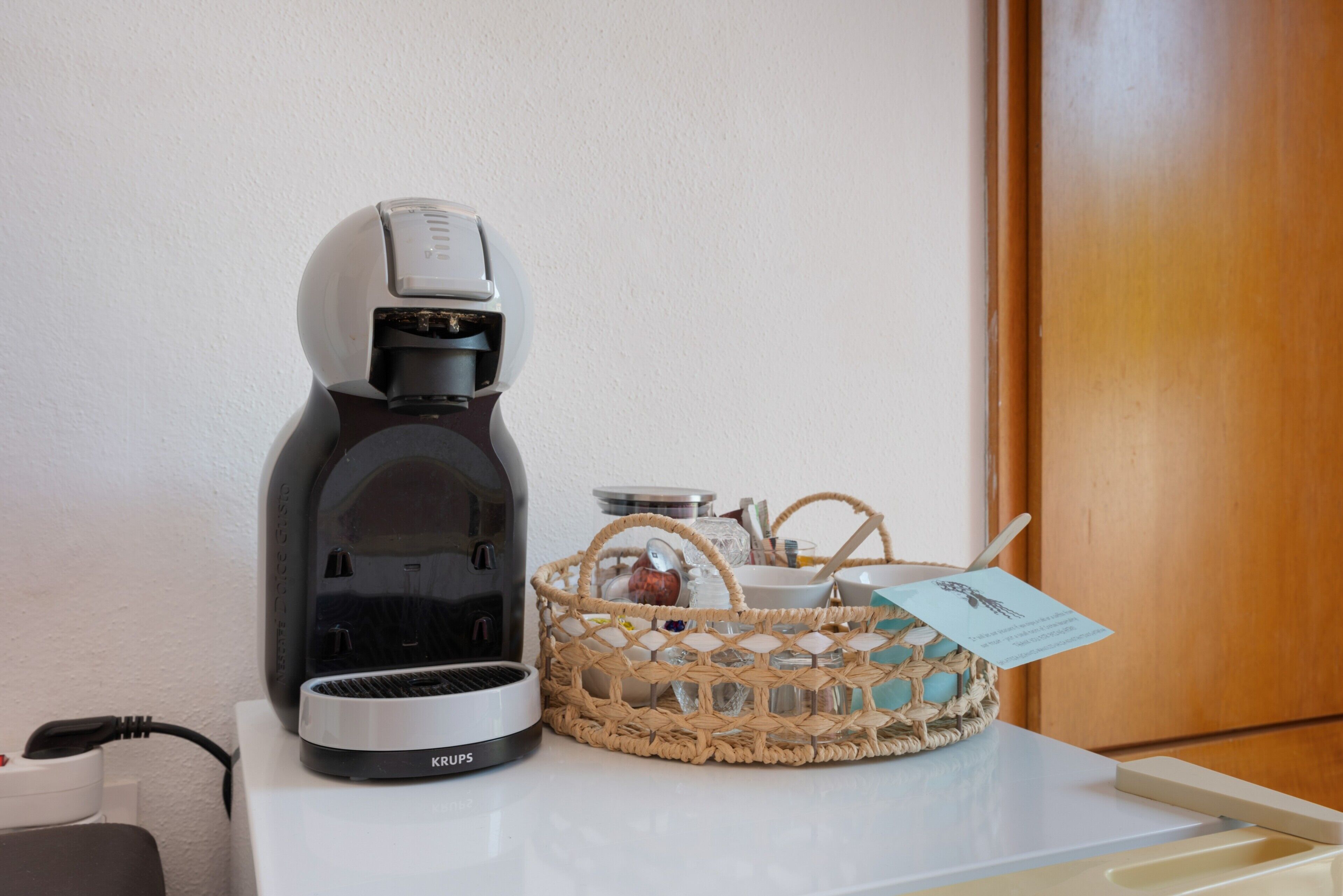 A coffee maker, a woven basket with a tag, and a white countertop.