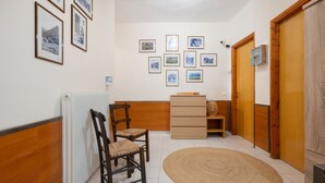A hallway with a radiator, wooden chairs, a woven rug, wooden doors, and framed pictures on the wall. - Room 'Artemis' with Wi-Fi (Lasithiou)