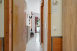 A hallway with wooden doors, a tiled floor, a bed, a desk, and a window with curtains.