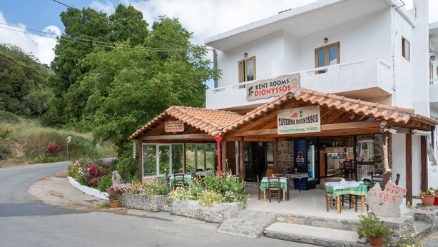 A white building with a sign for 'RENT ROOMS DIONYSOS' and 'TAVERNIA DIONYSOS' offering traditional food. - Room 'Artemis' with Wi-Fi (Lasithiou)