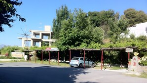 A parking area with a car, a building with a sign, and trees in the background. - Room 'Artemis' with Wi-Fi (Lasithiou)