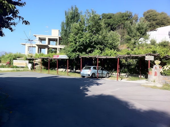 Un área de estacionamiento con un coche, un edificio con un letrero y árboles al fondo.