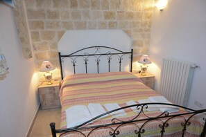 Un lit avec une couvre-lit à rayures, deux lampes de chevet, un radiateur et un mur en pierre.