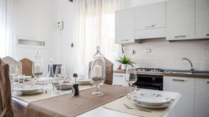 A dining area with a table set for four, a kitchen with modern appliances, and a window with sheer curtains. - Siqillya Etna Linguaglossa (Linguaglossa)