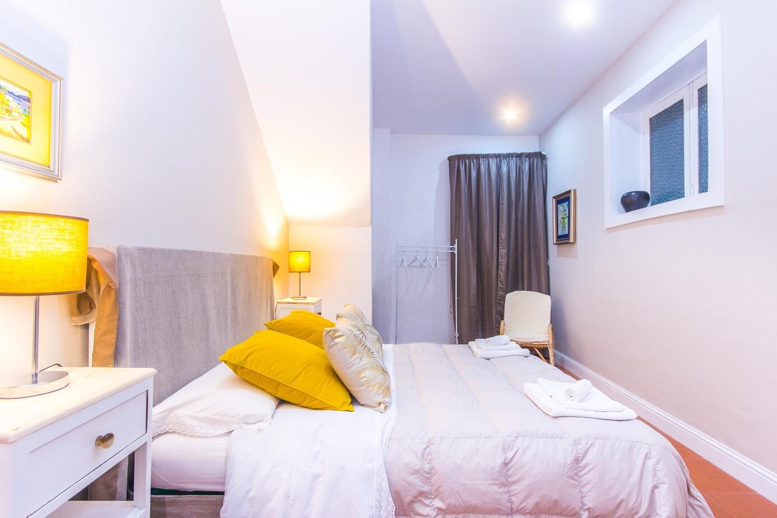 Une chambre d’hôtel avec un lit, des lampes de chevet, une fenêtre, une chaise et une porte.