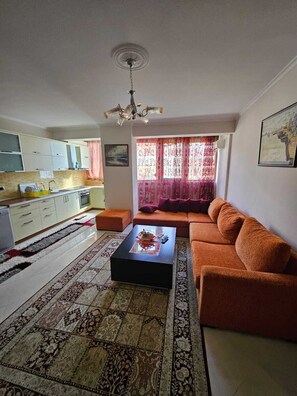 Ein Wohnzimmer mit einer Couch, einem Couchtisch, einem Teppich und einer Küche im Hintergrund sowie einem Deckenventilator.