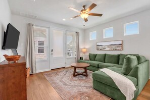 A living room with a green sofa, a wooden coffee table, a ceiling fan, and a television on a wooden cabinet. - Spring Haus Near Downtown (New Braunfels)