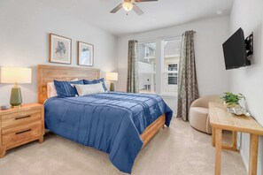 A bedroom with a bed, bedside tables, a ceiling fan, a TV mounted on the wall, and a window with curtains. - Spring Haus Near Downtown (New Braunfels)
