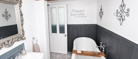 A bathroom with a white bathtub, a large mirror with an ornate frame, a wooden beam ceiling, and a decorative wall sign.