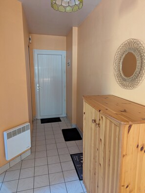 Un pasillo con una puerta blanca, un armario de madera y un espejo decorativo en la pared.