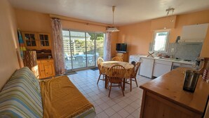 En kompakt opholdsstue med sofa, spisebord, stole, et tekøkken og en skydedør til terrassen.
