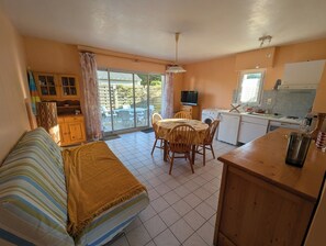 Un espacio habitable compacto con sofá, mesa de comedor, sillas, kitchenette y puerta corrediza al exterior.