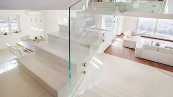 Un interior moderno con una escalera de cristal, zona de comedor, sala de estar y ventanas amplias.