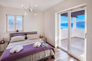 A bedroom with a bed, a nightstand, a bedside table, a window, and a view of the outdoors. - Pool Villa Royal Blue /w Panoramic Sea View (Rasa)