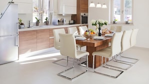 Una cocina moderna con armarios blancos, una isla de madera y una zona de comedor con una mesa grande y sillas.