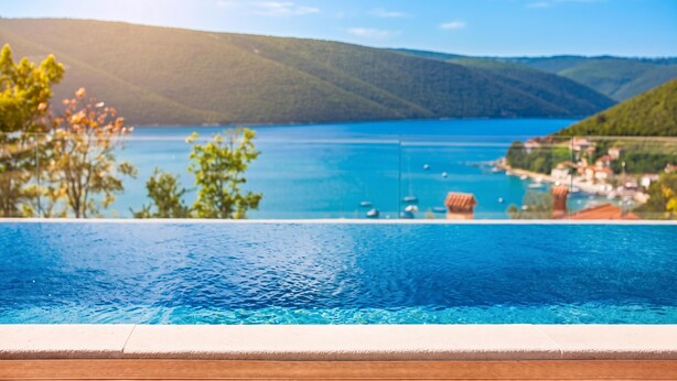 Piscina infinita con vistas a un lago con barcos y un pueblo.