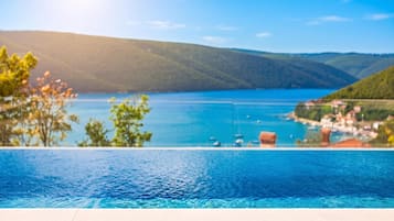 Piscina infinita con vistas a un lago con barcos y un pueblo.