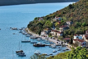A coastal village with boats docked along the shore, houses with red roofs, and a hilly backdrop. - Pool Villa Royal Blue /w Panoramic Sea View (Rasa)