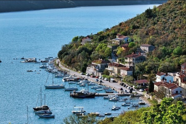 A coastal village with boats docked along the shore, houses with red roofs, and a hilly backdrop. - Pool Villa Royal Blue /w Panoramic Sea View (Rasa)