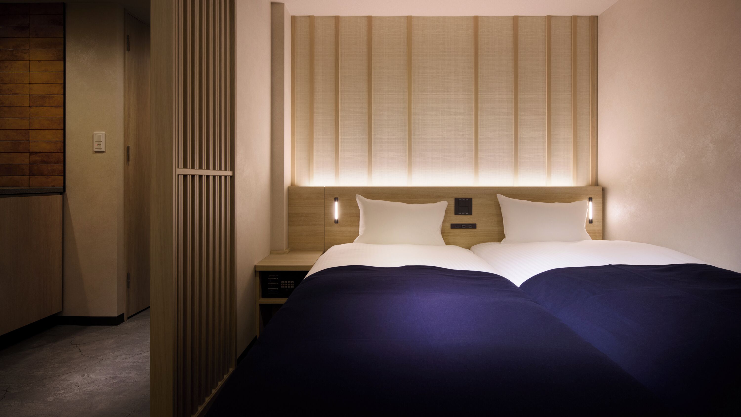 A hotel room with a bed, bedside tables, a wooden headboard, and a wall-mounted light fixture.