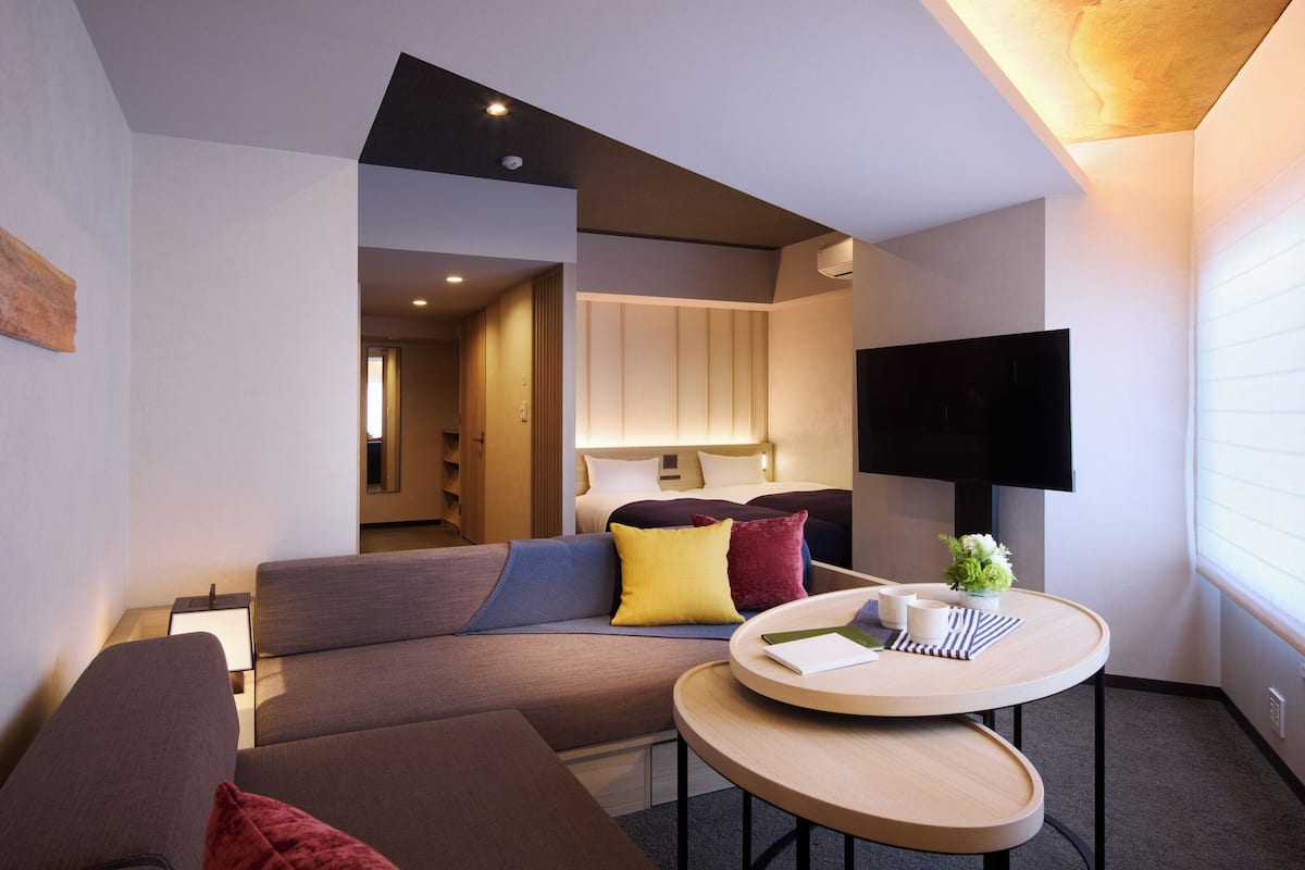 Una habitación de hotel moderna con sofá, una mesa redonda, televisión y vistas al exterior.