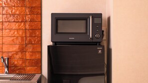 A kitchen with a black microwave on top of a black refrigerator, a stainless steel faucet, and a tiled backsplash. - Minn Namba South (Osaka)