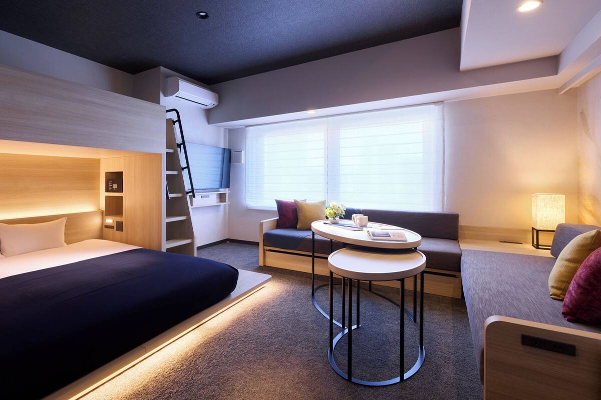 Una habitación de hotel moderna con cama, escritorio, silla, sofá y ventana con persianas.