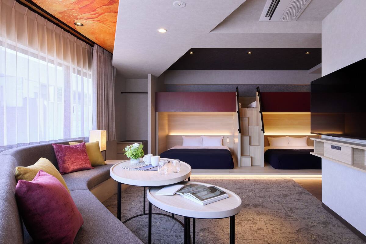 Una habitación de hotel moderna con sofá, una mesa redonda, cama y una escalera que lleva a un nivel superior.