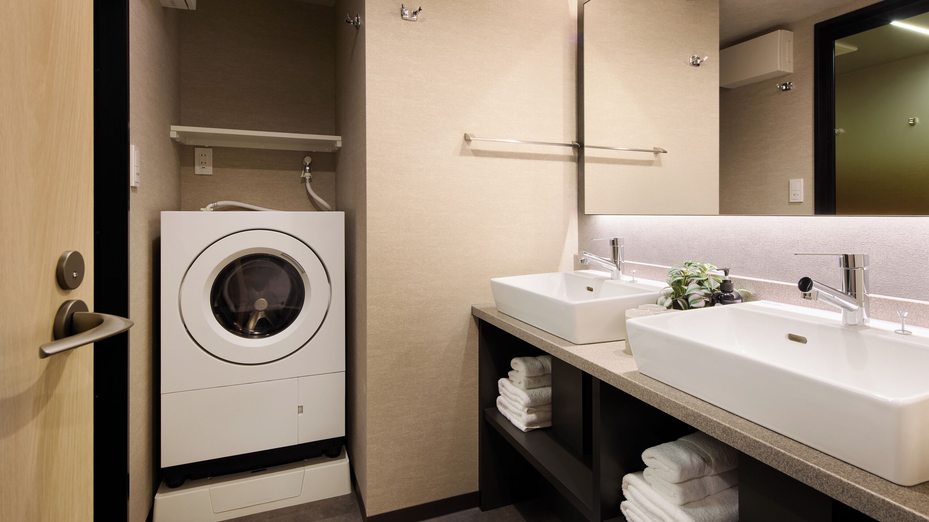 Un baño de hotel pequeño con lavadora integrada, dos lavamanos y un espejo.
