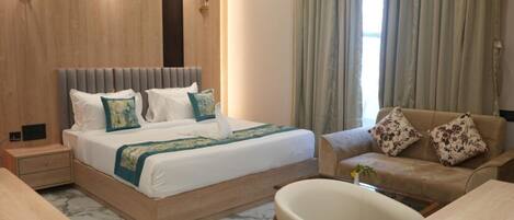 A hotel room with a bed, a sofa, a chair, a desk, and a nightstand.