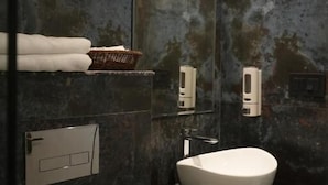 A modern bathroom with a large mirror, a white sink, a towel rack with towels, a basket, and soap dispensers. - Hotel Global Inn Keonjhar (Ghatagaon)