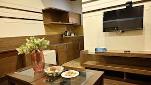 A modern kitchen with wooden cabinets, a glass-top table, a vase with flowers, and a flat-screen TV mounted on the wall. - Hotel Global Inn Keonjhar (Ghatagaon)