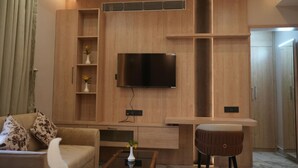 A modern living room with a flat-screen TV mounted on a wooden wall, a sofa, a coffee table, and a small stool. - Hotel Global Inn Keonjhar (Ghatagaon)