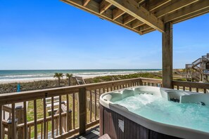 Eine Holzterrasse mit Whirlpool mit Blick auf einen Strand.