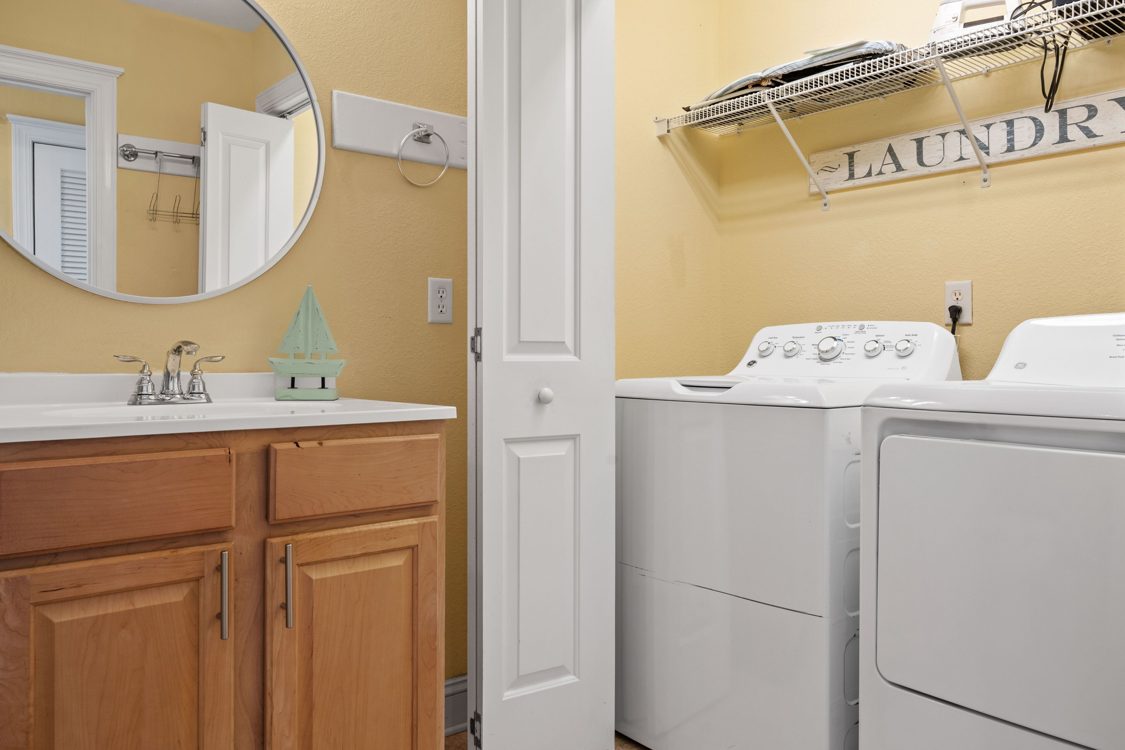 A bathroom with a sink, mirror, wooden cabinets, a door, and a laundry area with a washing machine and dryer.