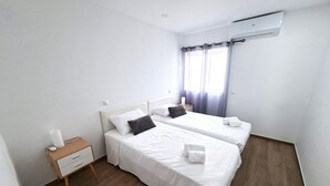 Una camera d'albergo con due letti, un comodino, una lampada e un condizionatore.